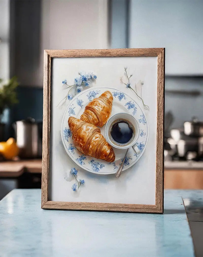 A delicate illustration of two croissants and a cup of coffee on a blue floral plate. Perfect wall art for creating a cozy, French café atmosphere in your kitchen or dining area