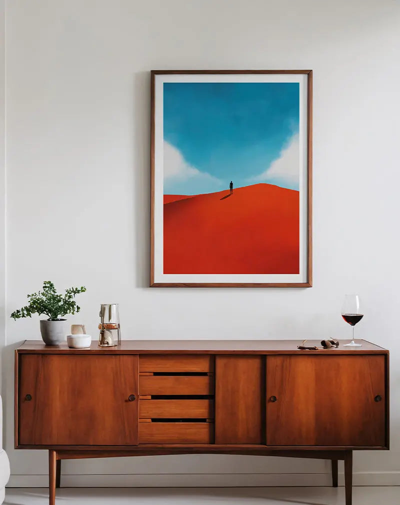 A minimalist illustration of a lone figure standing on a red sand dune under a vast blue sky. The bold color contrast between the vibrant red and serene blue creates a striking visual effect. Perfect wall art for evoking a sense of solitude and wonder in contemporary or minimalist spaces.